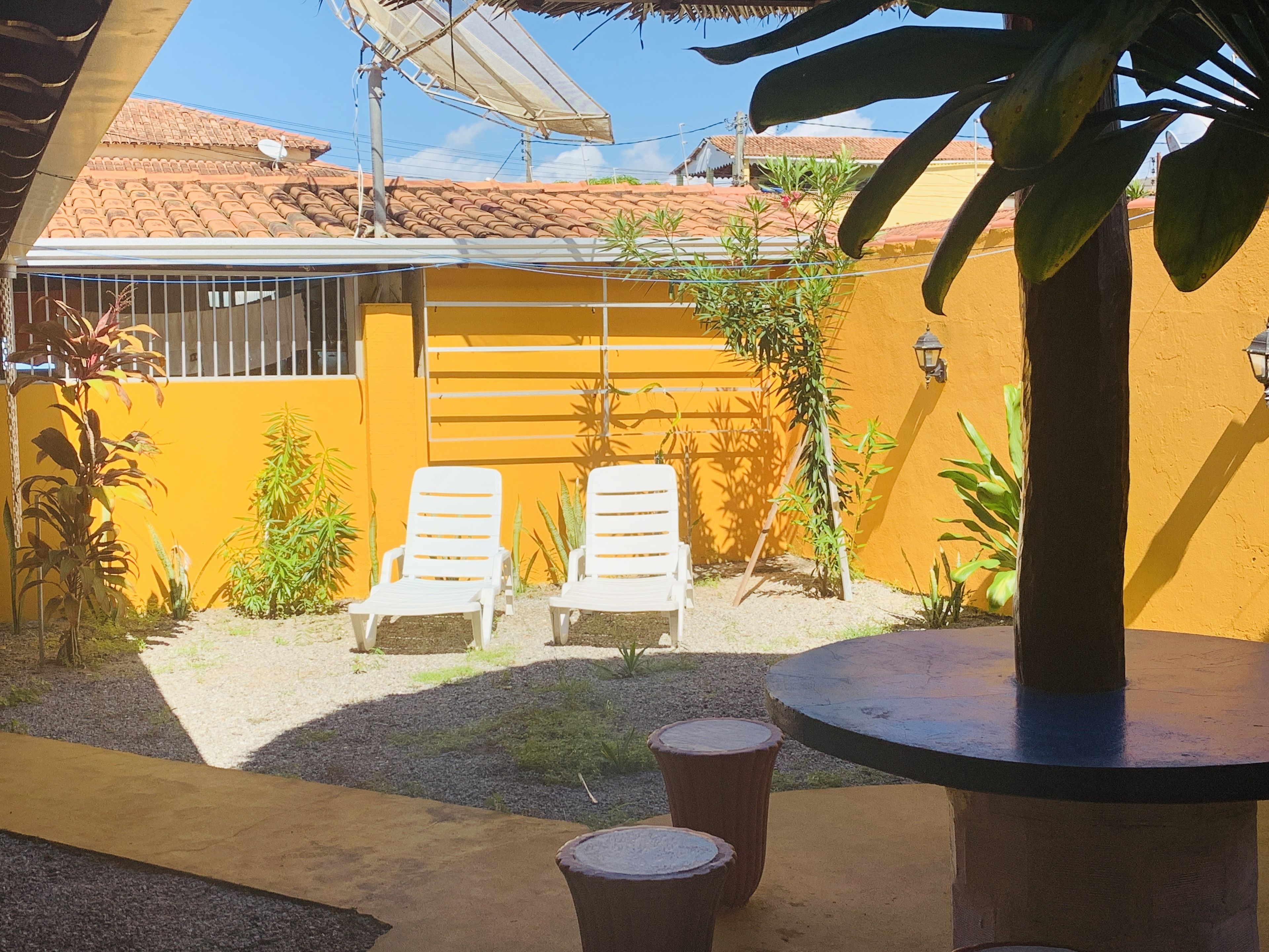 Un patio con dos sillones blancos, una mesa redonda y un taburete de madera.