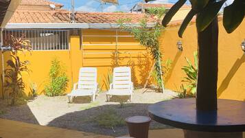 Un patio con dos sillones blancos, una mesa redonda y un taburete de madera.