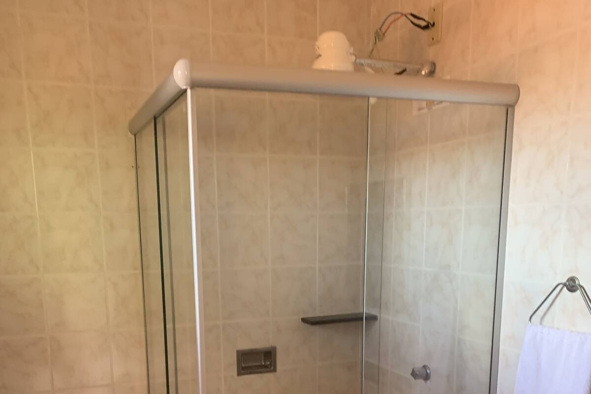 A glass-enclosed shower stall with a toilet to the left and a sink with a towel hanging on the wall to the right.