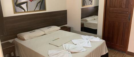 A hotel room with a bed, a nightstand, a mirror, and a wooden door.