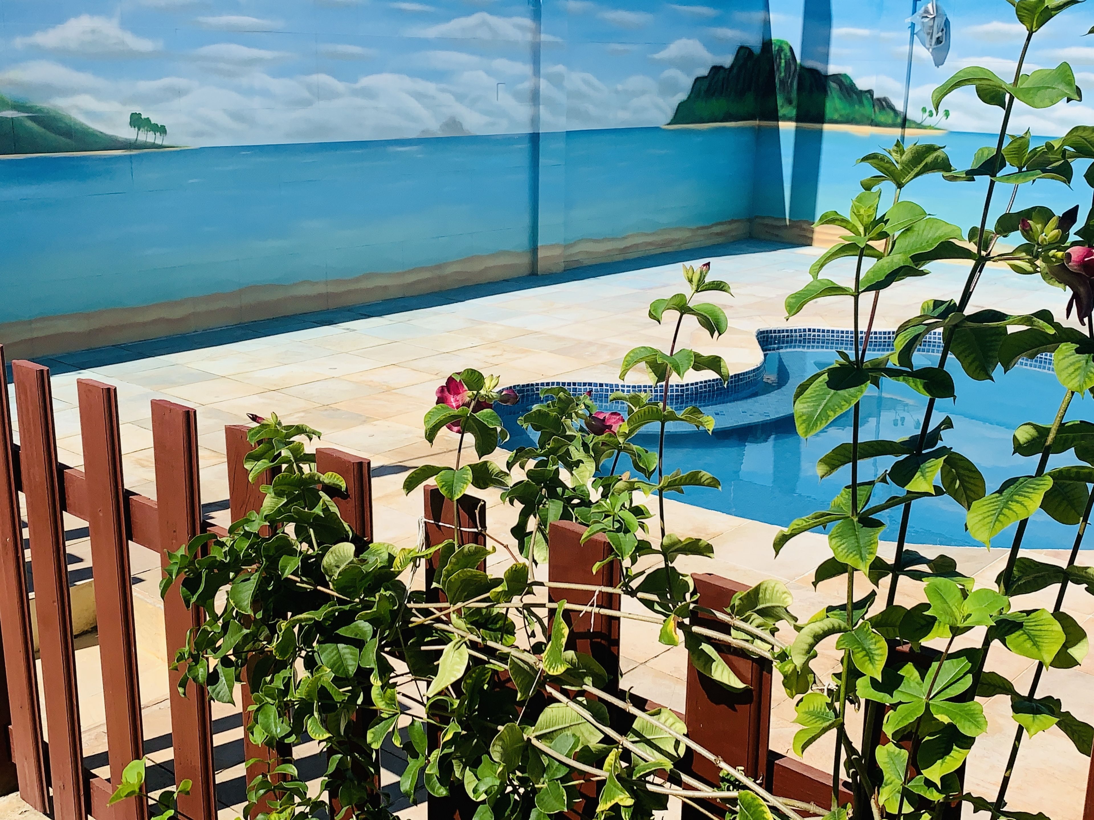 A swimming pool with a tiled deck, surrounded by a wooden fence and lush green plants.