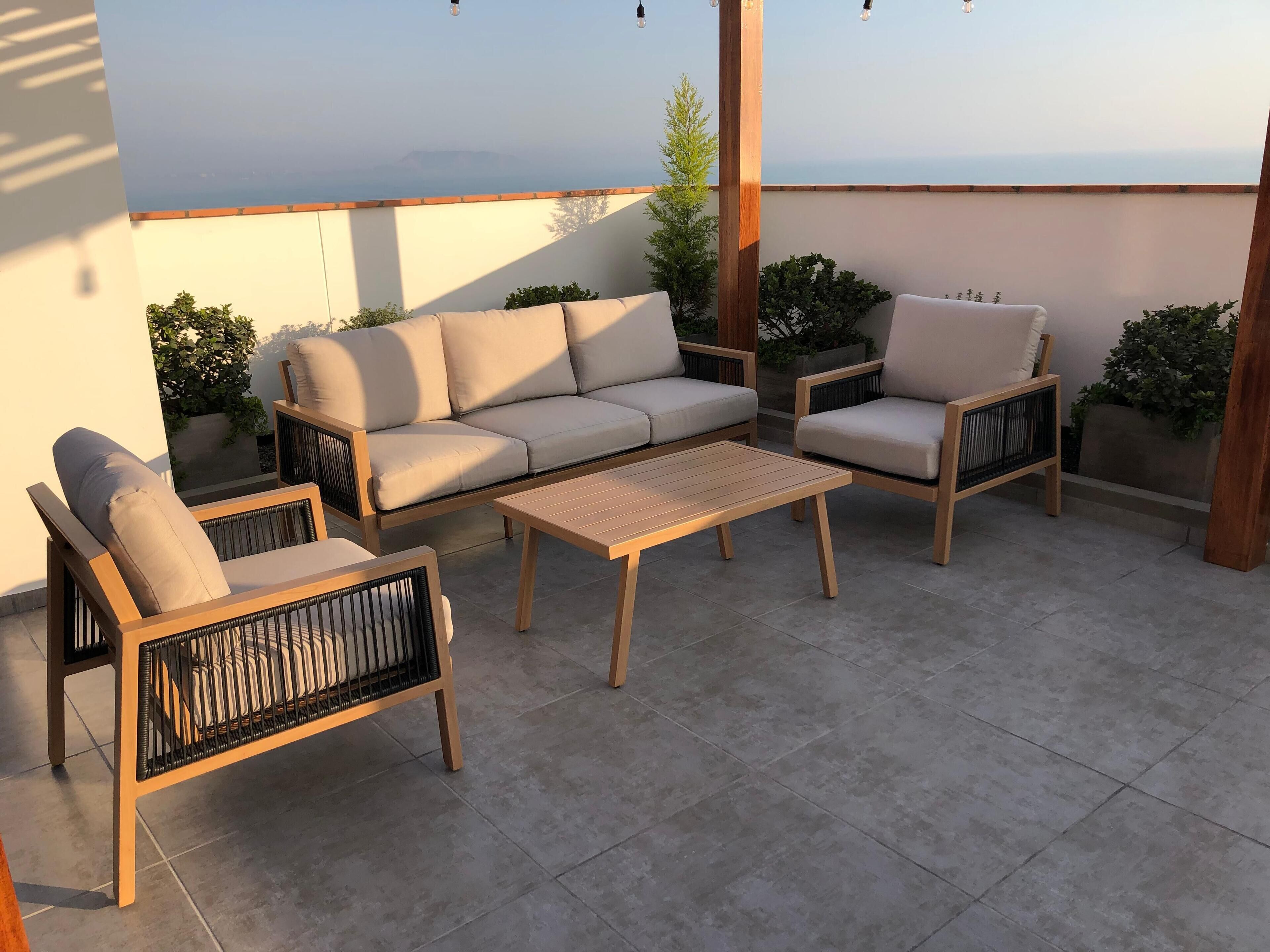 Un patio con un divano color beige, due poltrone e un tavolino in legno.