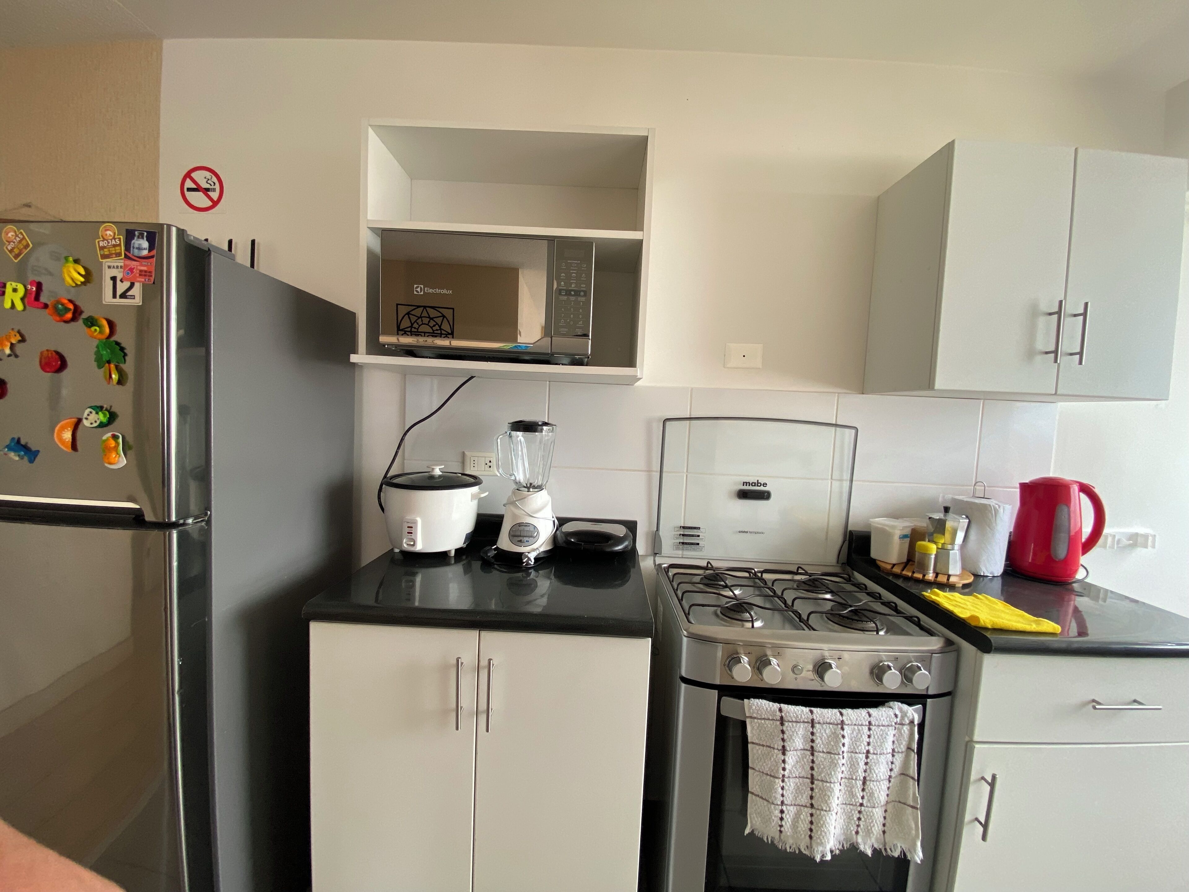 A kitchen with a refrigerator, microwave, stove, and a blender on the counter.