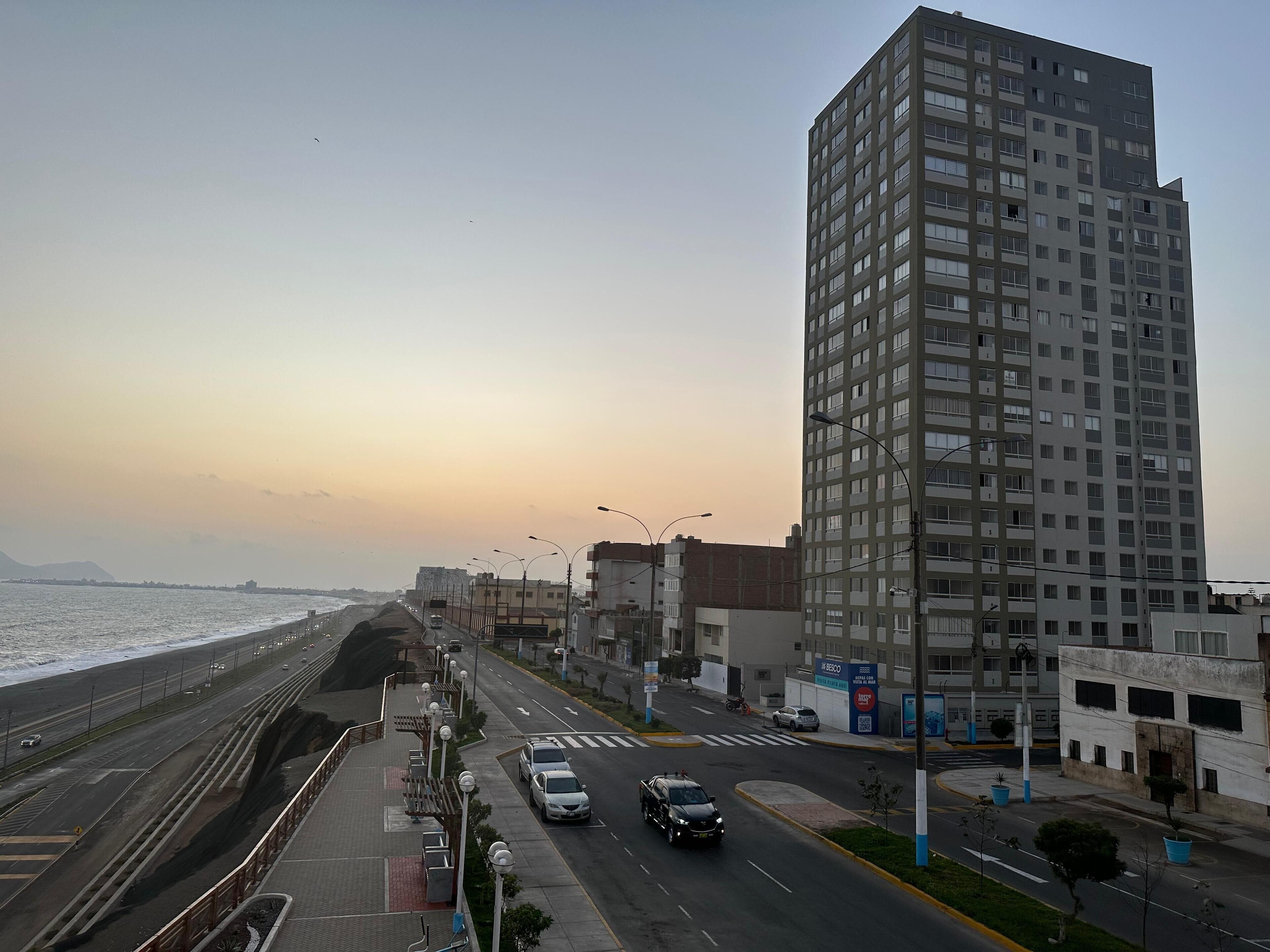 A coastal road with a high-rise building, a pedestrian walkway, and a view of the sea.
