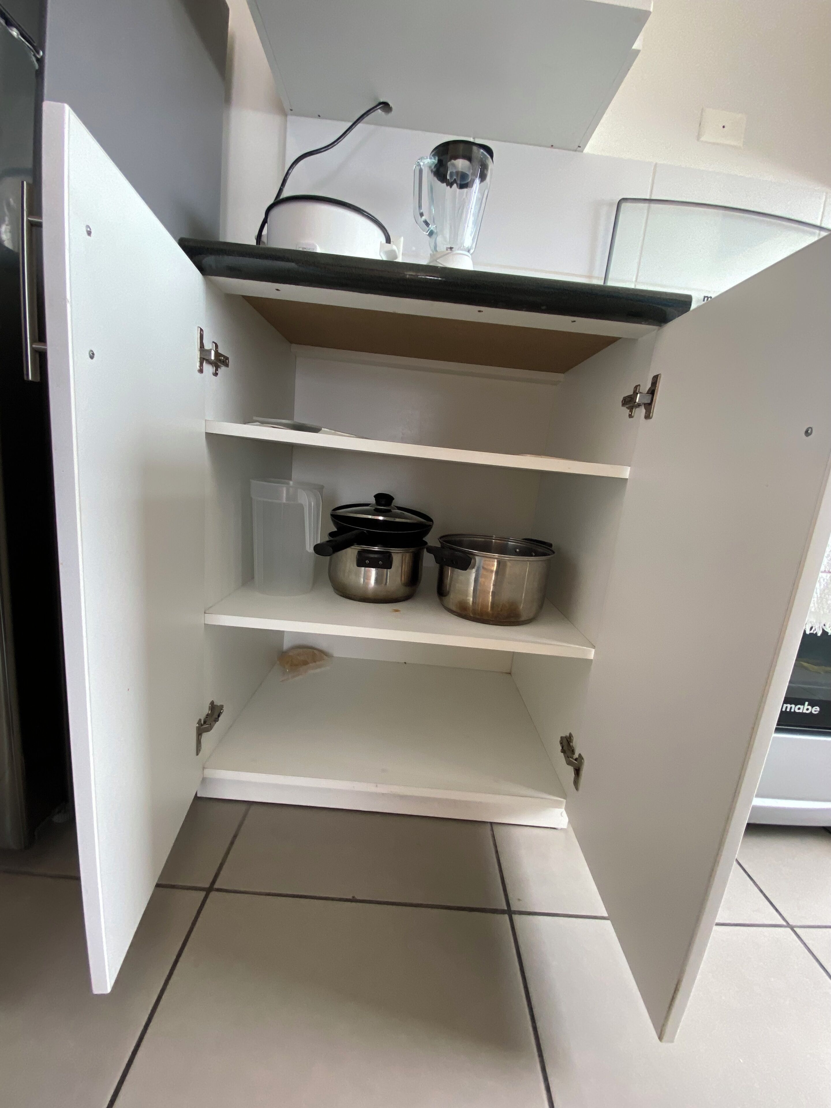 Un meuble de cuisine ouvert, avec deux casseroles en acier inoxydable sur l’étagère du milieu et un mixeur sur l’étagère supérieure.