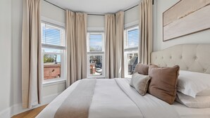 Une chambre avec un grand lit, des rideaux de couleur beige et une vue sur la ville.