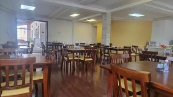 Uma sala de jantar com várias mesas e cadeiras de madeira, um pilar de pedra e vista para o exterior.