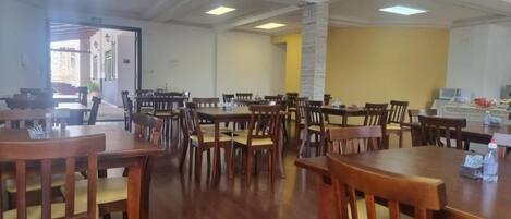 A dining area with multiple wooden tables and chairs, a stone pillar, and a view of the outside.