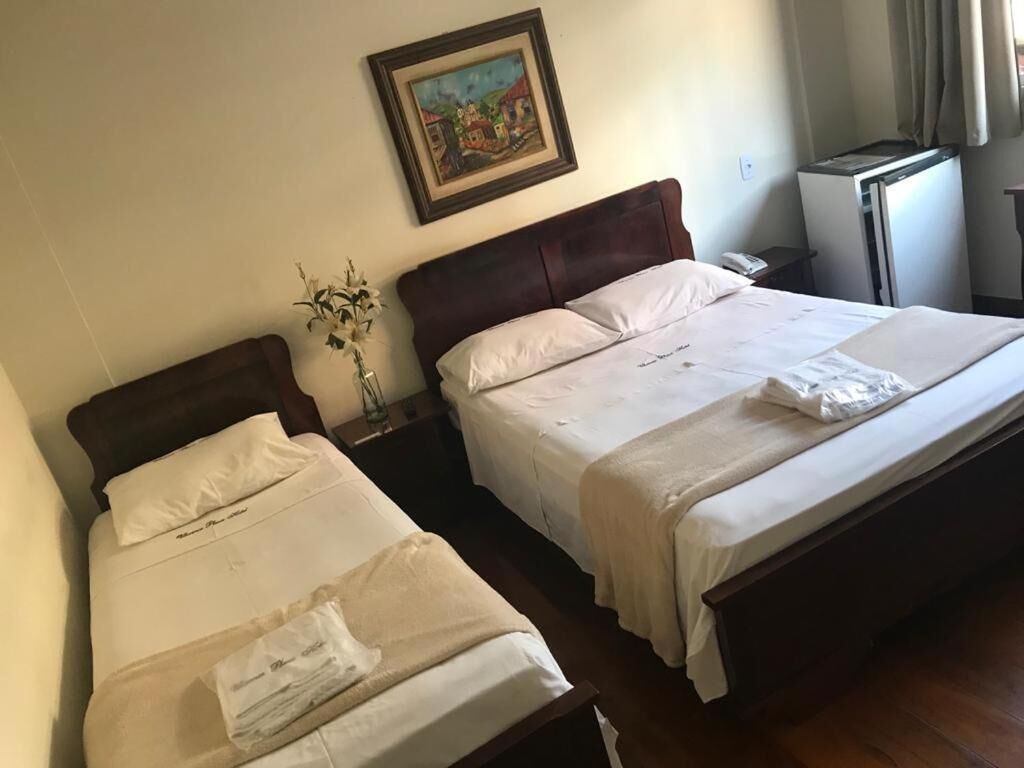 A hotel room with two single beds, a nightstand, a small table, a refrigerator, and a painting on the wall.