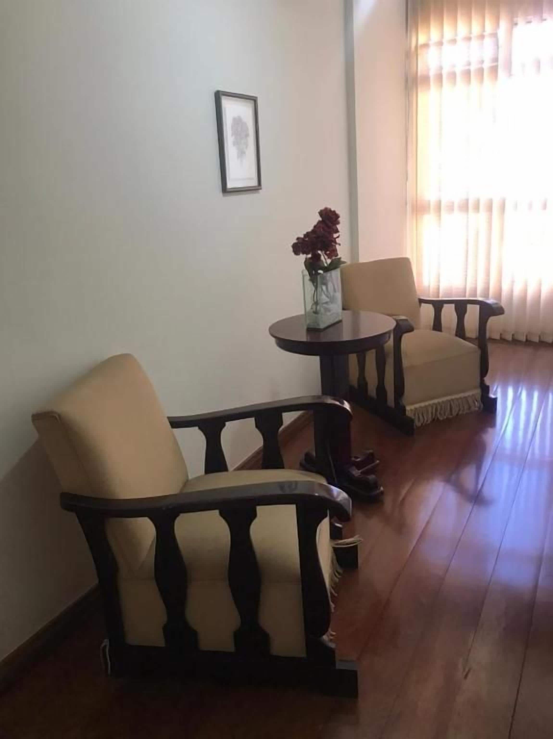A room with two chairs and a small table, a framed picture on the wall, and a window with curtains.