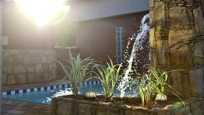 A stone fountain with water spouting from the center, surrounded by plants and a pool. - Ubaense Plaza Hotel (Uba)