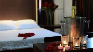 A hotel room with a bed, a bedside table with a champagne bottle, and a vase of red flowers. - Ubaense Plaza Hotel (Uba)