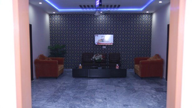 A modern living room with a flat-screen TV mounted on the wall, two sofas, a coffee table, and patterned wallpaper. - Family Hotel Lahore  (Block R 2)