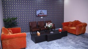 A reception area with patterned wallpaper, a television, three leather chairs, an orange sofa, and a marble coffee table. - Family Hotel Lahore  (Block R 2)