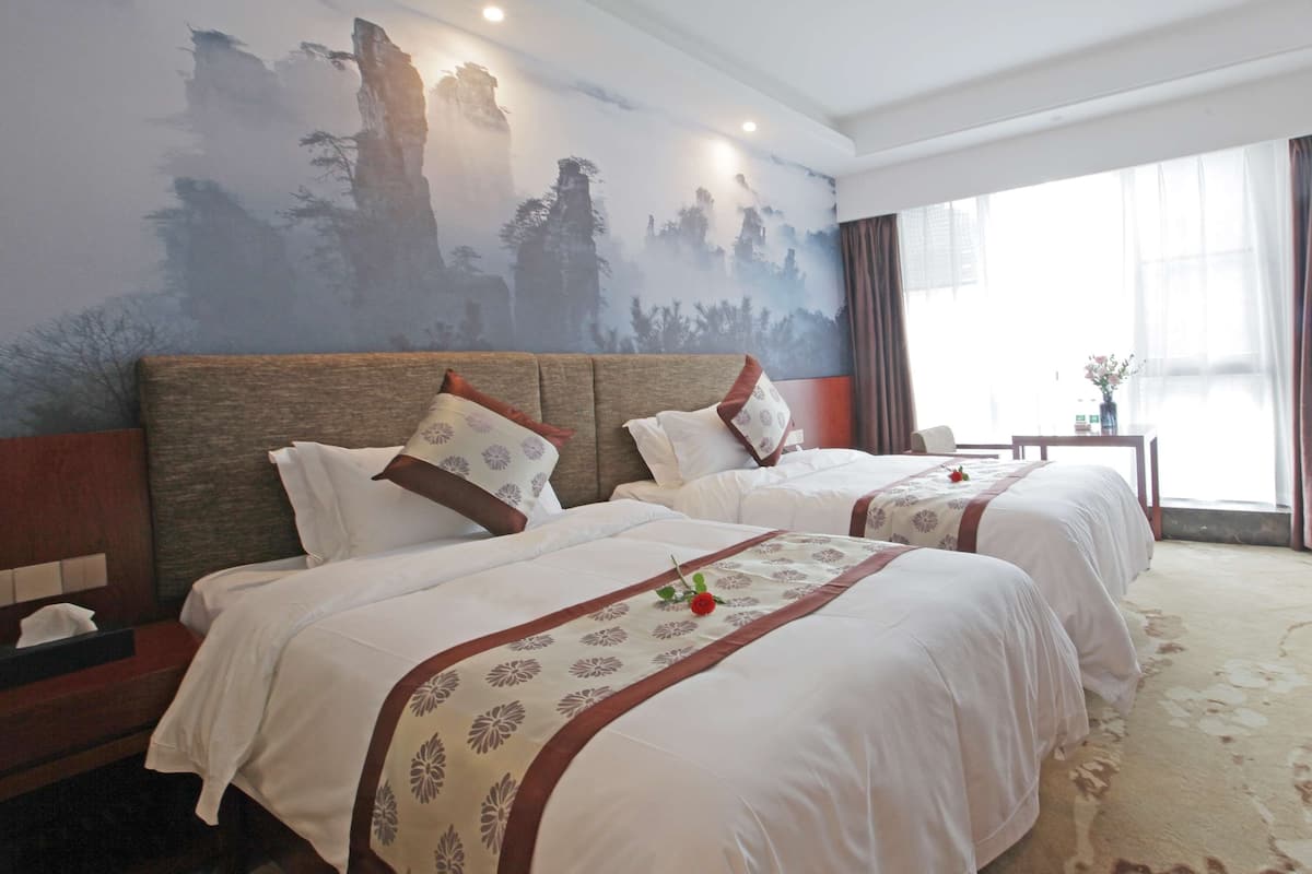A hotel room with two beds, a nightstand, a small table, and a large window with curtains.