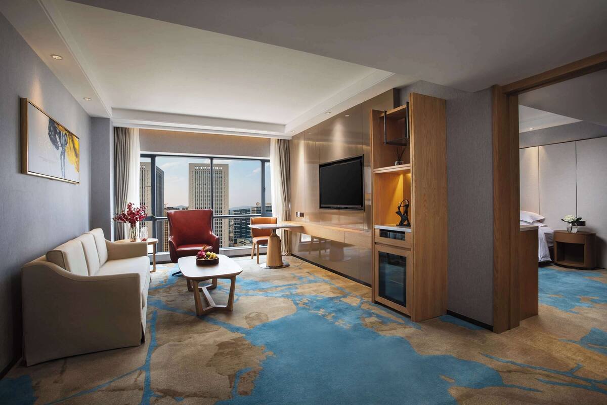 Ein modernes Hotelzimmer mit einem großen Fenster, einem Sofa, einem roten Sessel, einem Couchtisch und einem Fernseher.