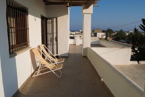 Ein Balkon mit Blick auf das Meer, eine weiße Wand und ein Metallgitter.