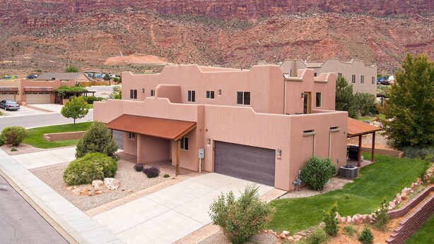 A modern two-story house with a flat roof and stucco exterior, surrounded by a well-maintained lawn and a mountain backdrop. - Southgate 2 by MoabCondos4Rent (Moab)