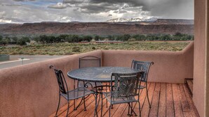 A patio with a round metal table and four chairs, overlooking a mountainous landscape with a road and sparse vegetation. - Southgate 2 by MoabCondos4Rent (Moab)
