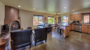 A spacious living area with a fireplace, leather seating, a dining table, and a kitchen with wooden cabinets and a dishwasher. - Southgate 2 by MoabCondos4Rent (Moab)