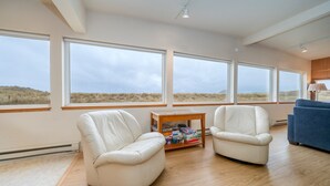 A spacious living room with large windows, a blue sofa, and two white armchairs. - Beachfront Home, on the Sand and Pet Friendly! (Pacific City)