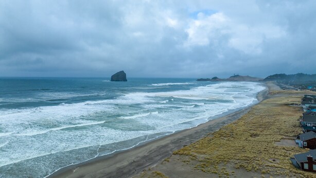 A coastal view with a beach, ocean waves, and a distant rock formation. - Beachfront Home, on the Sand and Pet Friendly! (Pacific City)