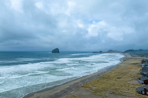 A coastal view with a beach, ocean waves, and a distant rock formation.