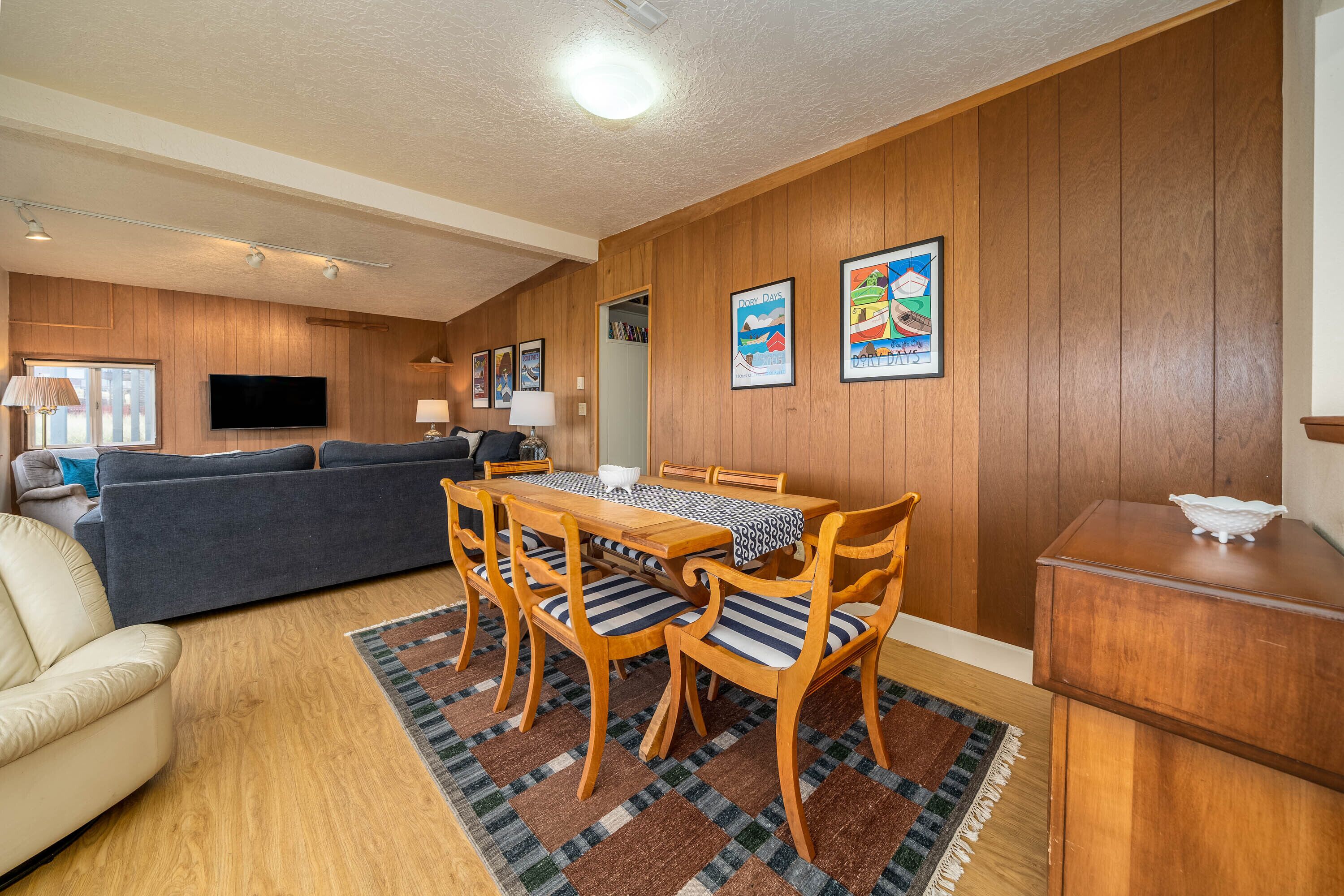 Un salon avec un mur lambrissé en bois, un téléviseur à écran plat, un canapé, une table à manger avec des chaises et un tapis.