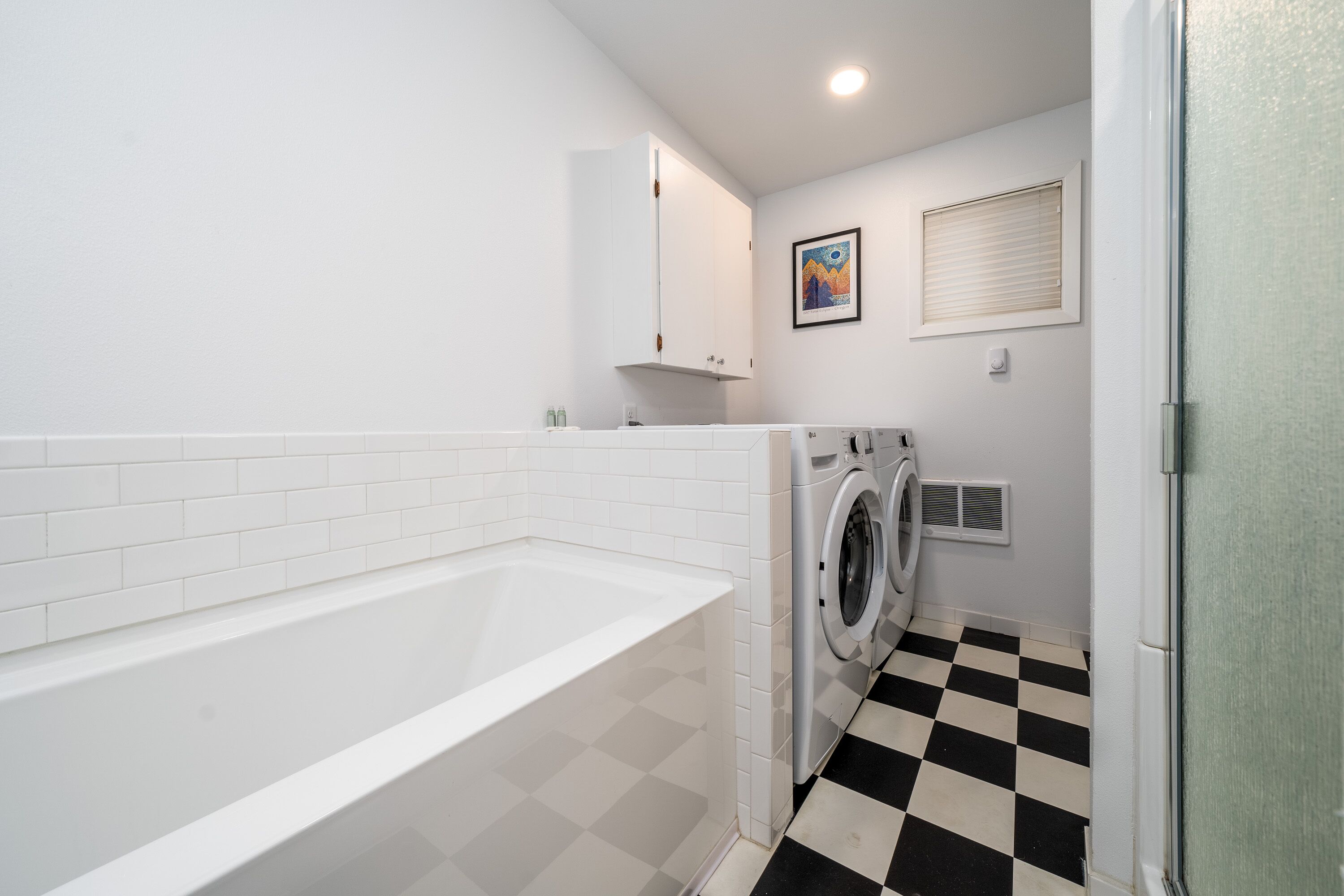A laundry room with a white bathtub, a washing machine, and a checkered floor.