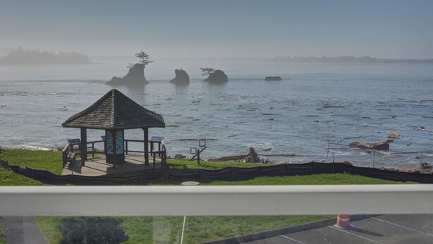 A gazebo with a roof and a bench, located near a body of water with visible rocks.