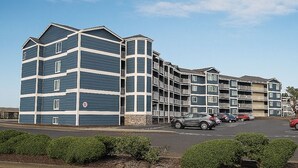 A multi-story hotel with a modern architectural design, featuring balconies and a parking lot with several cars.
