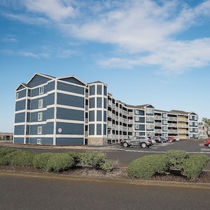 A multi-story hotel with a modern architectural design, featuring balconies and a parking lot with several cars.