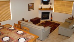 A living room with a fireplace, a television, a dining table set for four, and a sofa. - Tierra Del Sol 1 by MoabCondos4Rent (Moab)