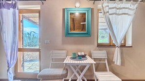 A small room with a wooden ceiling, a table with two chairs, a framed mirror, and a window with curtains.