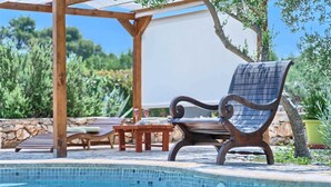 A poolside area with a lounge chair, a pergola, and a stone wall.