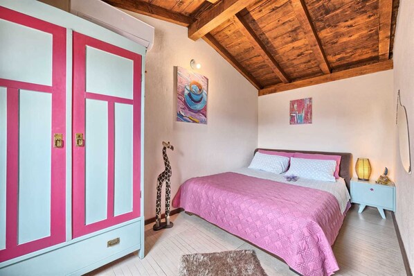 A bedroom with a bed, a wardrobe, and a ceiling with wooden beams.