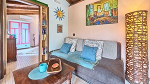 A cozy living room with a wooden ceiling, a colorful painting, a woven lamp, and a bookshelf.