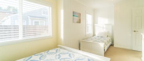 Quarto com duas camas, uma janela com persianas, um quadro na parede e uma porta.