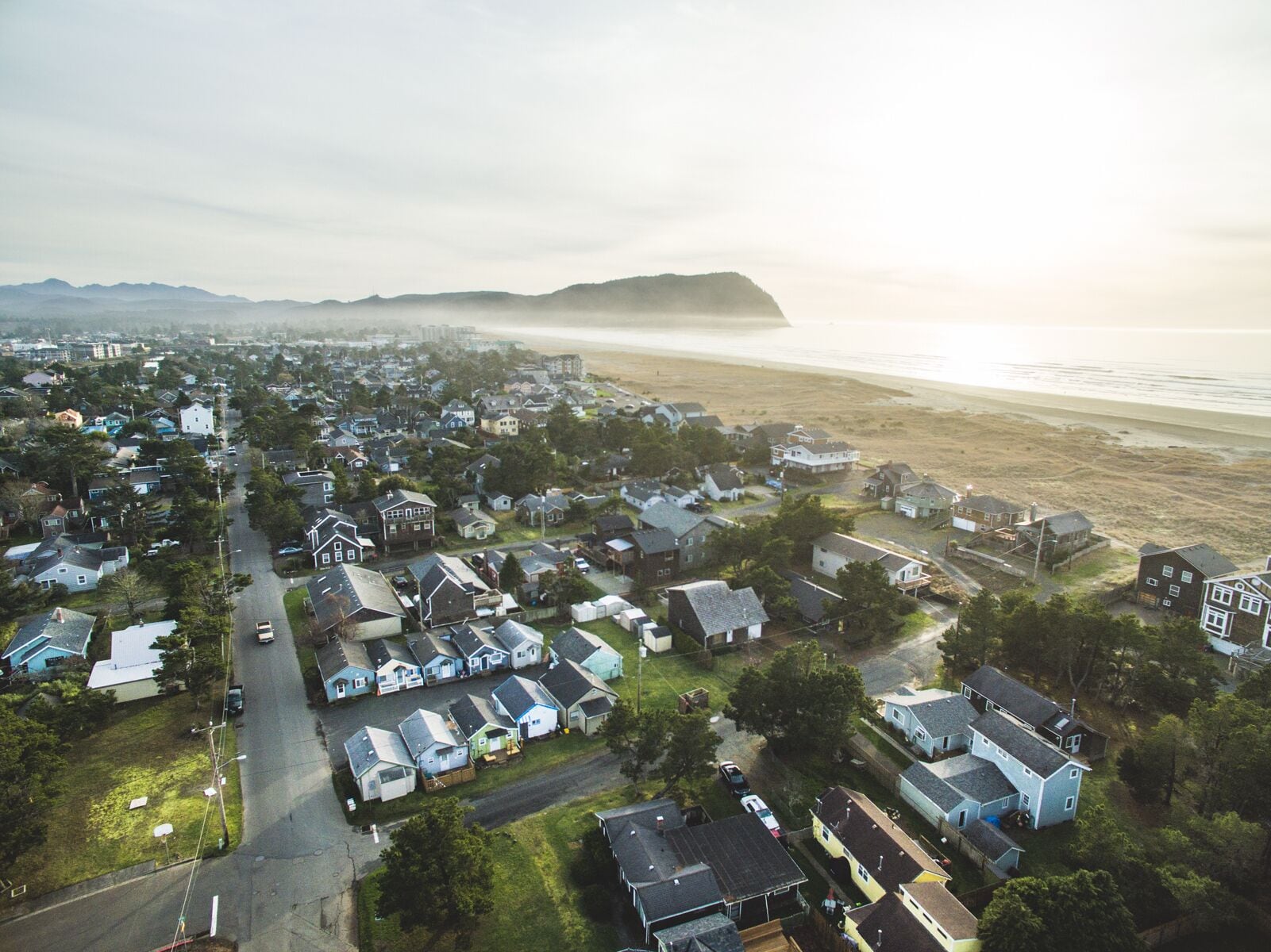 An aerial view of a coastal residential area with houses, a road, and a beach.
