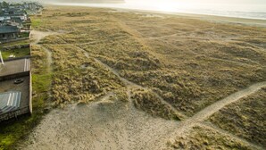 Une zone côtière comprenant une plage de sable, des dunes herbeuses et un quartier résidentiel avec des maisons.