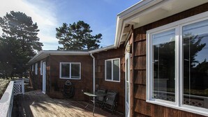 Une terrasse en bois avec une table et des chaises, un patio couvert et une grande fenêtre sur le côté droit.