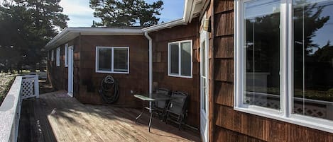 Une terrasse en bois avec une table et des chaises, un patio couvert et une grande fenêtre sur le côté droit.