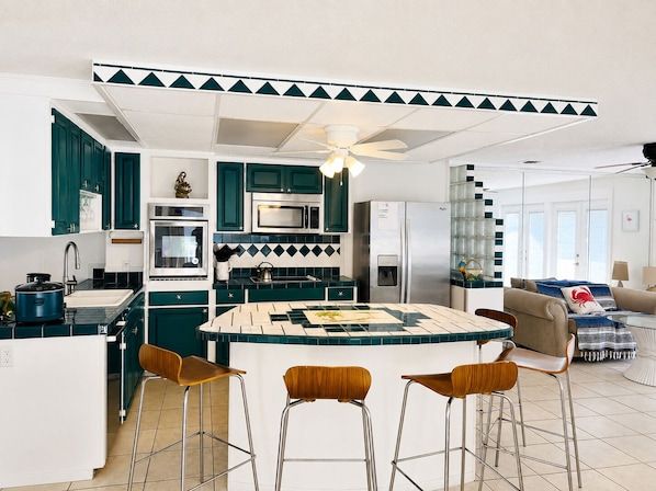 A modern kitchen with a central island, bar stools, and a refrigerator.