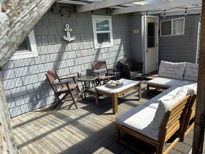 A sunlit patio with a wooden table, two chairs, a wicker chair, and a sofa with cushions.