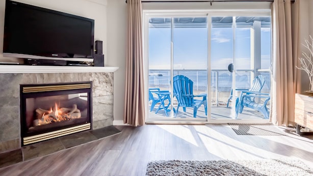 Ein Wohnzimmer mit Kamin, Flachbildfernseher und einer großen Schiebeglastür, die auf einen Balkon mit blauen Stühlen führt.