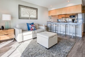 A modern living room with a sofa, ottoman, and a kitchen area with a bar.