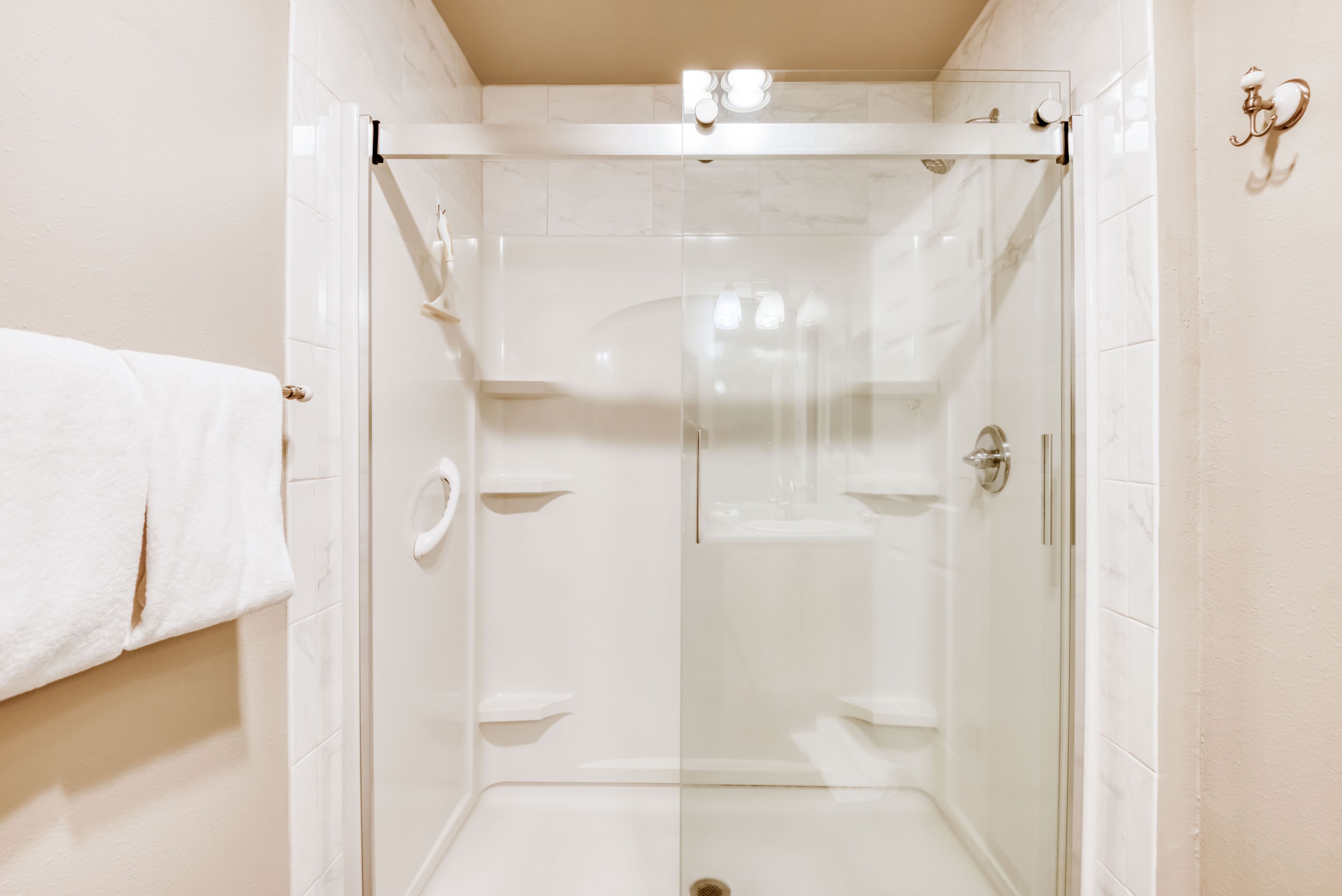 A glass-enclosed shower stall with a white tiled wall and a towel hanging on the wall.