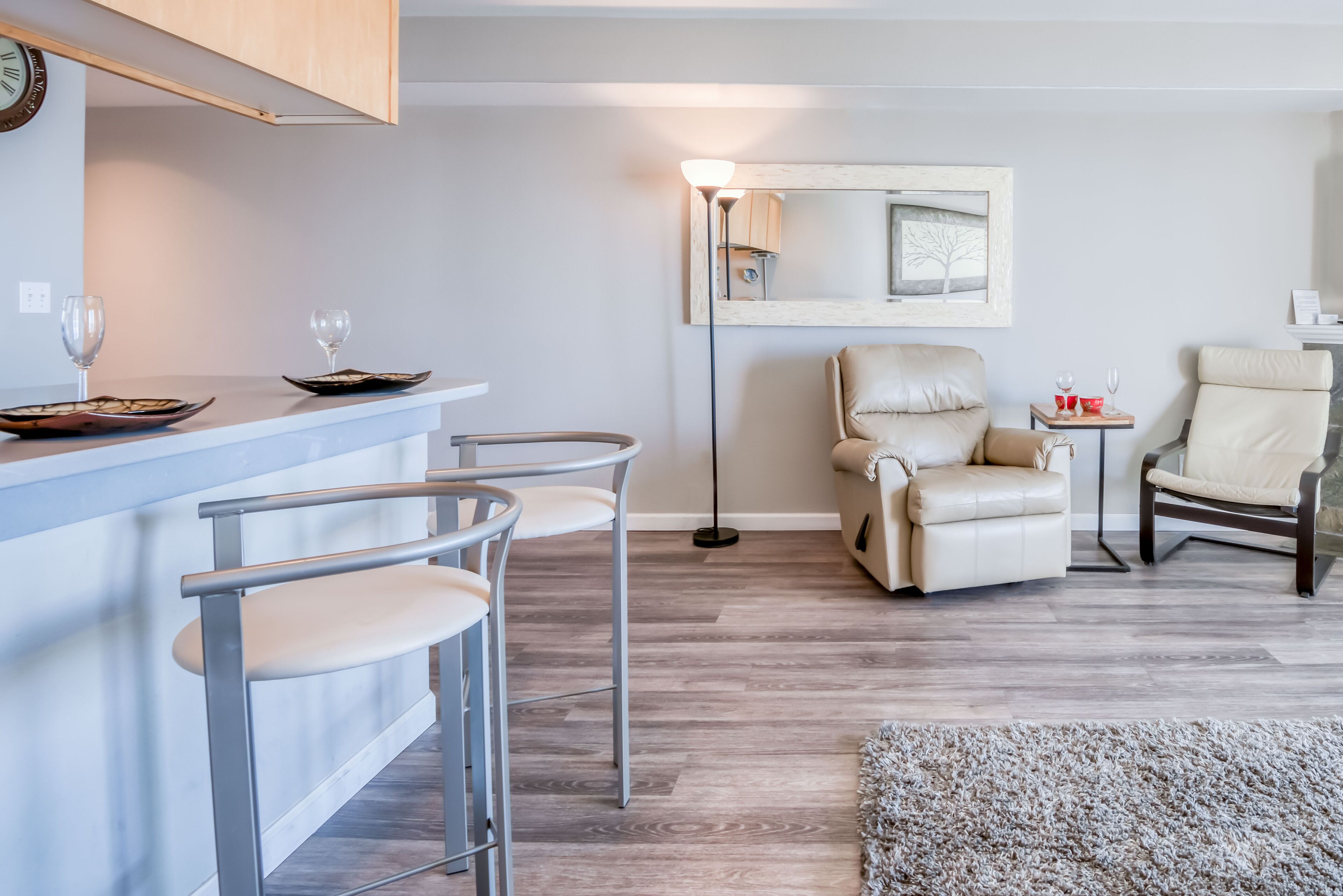Een moderne woonkamer met een bar, twee leren fauteuils, een grote spiegel en een vloerlamp.