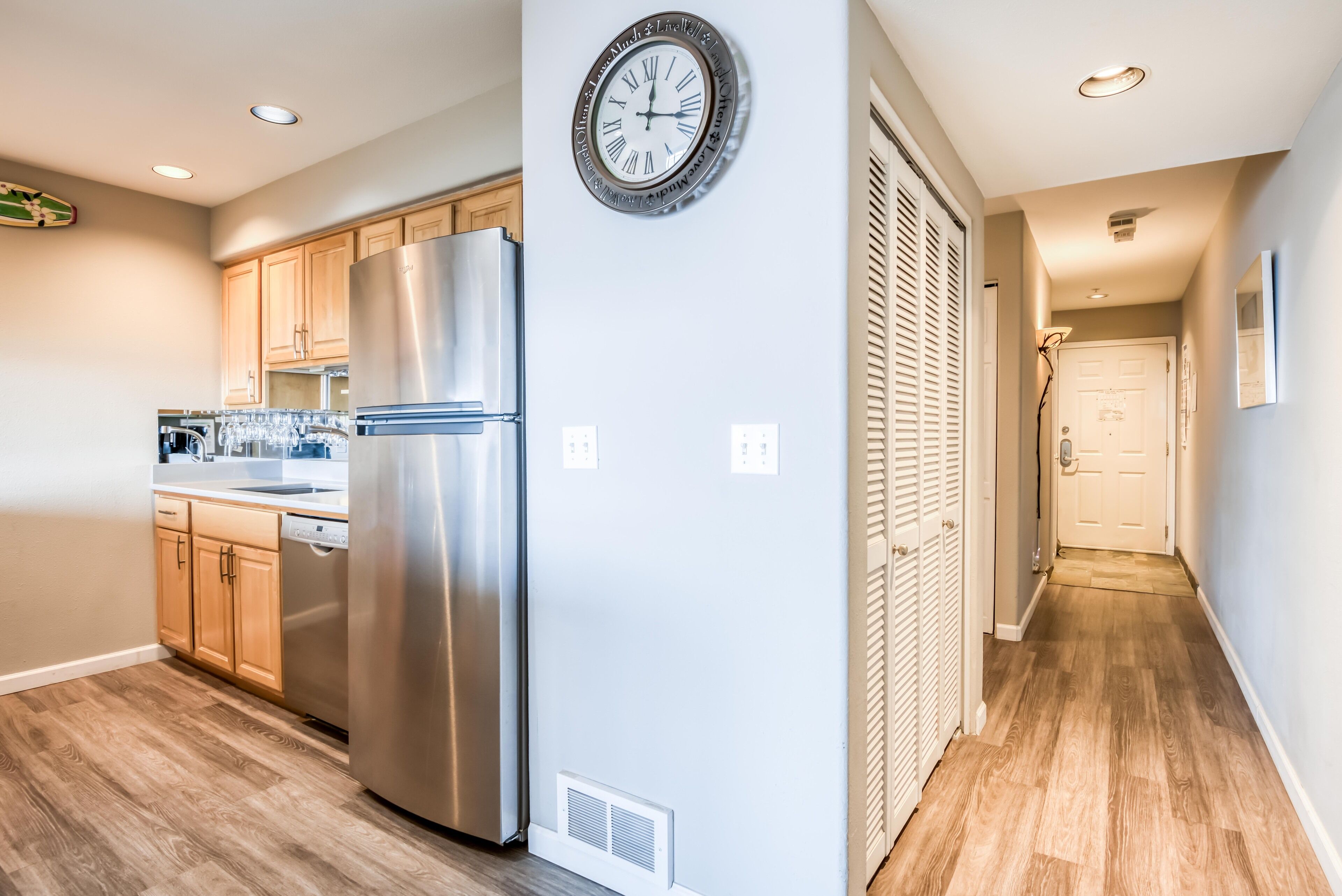 A modern kitchen with stainless steel appliances, wooden cabinets, and a wall clock.