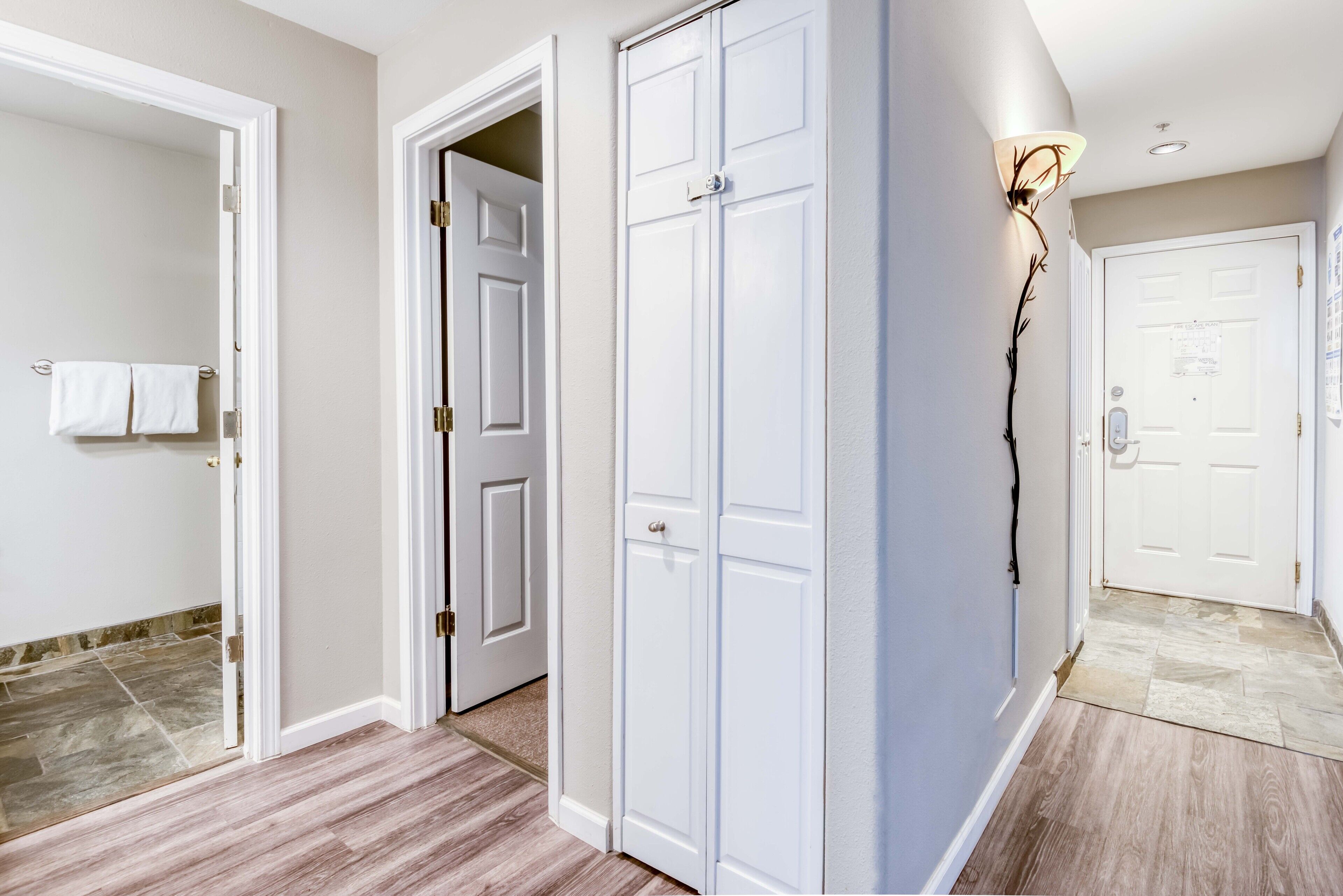 A hallway with white double doors, a light fixture on the wall, and a tiled floor.